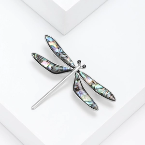 Elegant silver dragonfly brooch with iridescent abalone shell wings on white platforms