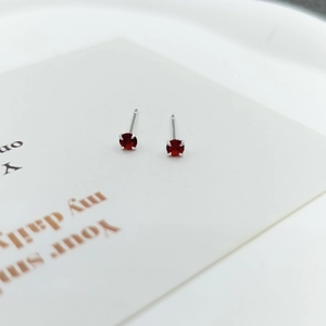 Close-up of elegant small red zircon stud earrings with silver four-prong setting