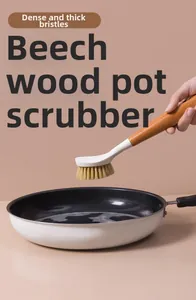 Detail of long-handled beech wood kitchen brush cleaning a frying pan with dense bristles