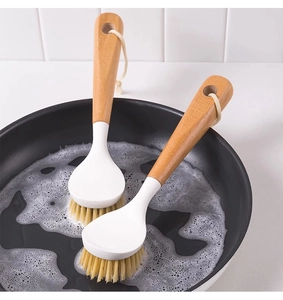 Two long-handle wooden kitchen brushes with dense bristles in a soapy black frying pan