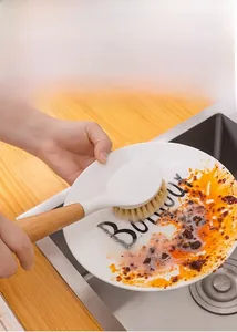 Long handle wooden cleaning brush scrubbing a dish in a kitchen sink with water