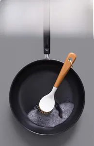 Kitchen dish brush with beech wood long handle scrubbing soap suds in a black frying pan