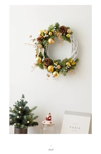 Close-up of a white wicker Christmas wreath with gold ornaments and pine cones on a wall