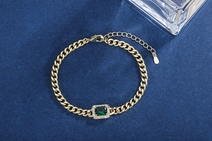 Macro view of gold Cuban bracelet with emerald green gem and lobster clasp closure