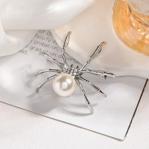 Macro di una spilla a ragno argentata con perla bianca e strass brillanti sulla testa