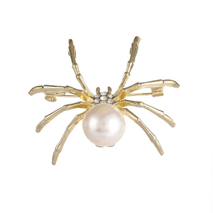 Elegante spilla a ragno dorata con una grande perla bianca e strass brillanti su bianco