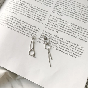 Detail of silver asymmetric earrings with circles and long tassels on a vintage book