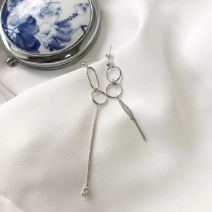 Detailed view of asymmetric silver earrings on white silk fabric with ceramic decor