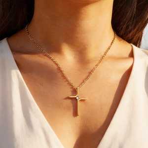 Detailed macro view of a minimalist gold cross necklace with a sparkling zircon pendant