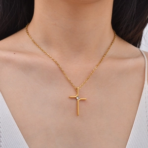 Detail shot of a minimalist gold cross pendant necklace with a clear center stone