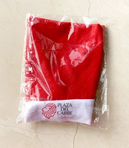 Detail of a red Christmas hat with white Plaza del Caribe logo in plastic packaging