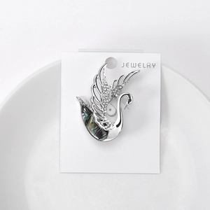Close-up of crystal swan brooch with shimmering abalone shell inlay on white tray