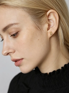 Close-up of golden infinity stud earrings with sparkling zircon stones on female ear
