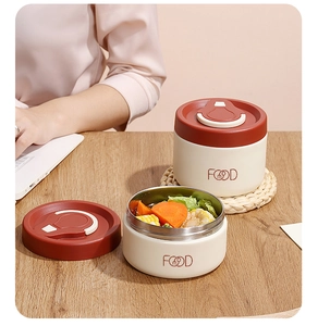 Detail of insulated cream lunch jars with red lids and foldable handles on a wooden table