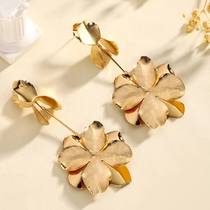 Close-up of oversized golden flower tassel earrings with brushed metal finish