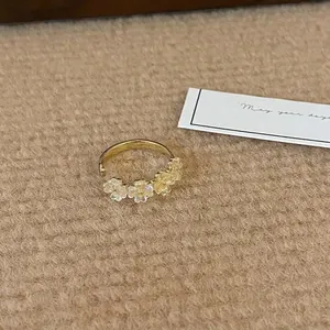 Exquisite gold open ring with small pearl flower accents on a textured camel fabric background