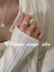 Detail of silver twisted knot ring set and pearl necklace on cream ribbed knitwear