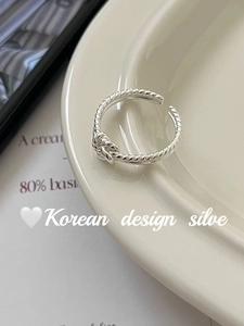 Detail of twisted knot open ring in S925 silver on a cream ceramic plate