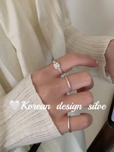 Detailed view of three-piece silver knot rings worn on finger with knit sweater background