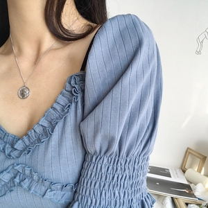 Detailed view of the silver coin pendant necklace styled with a blue knit top