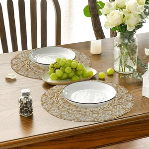 Detailed view of round linen placemats with gold mandala prints on a wooden dining table