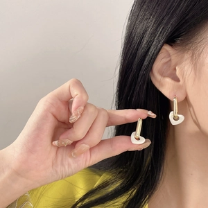 Elegant gold-tone heart drop earrings with white ceramic charms worn by a model
