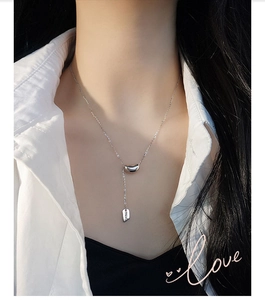 Detail of 925 sterling silver bean pendant necklace with square tag on a female model