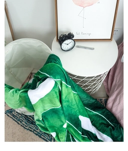 Detail of soft flannel blanket featuring vibrant green tropical leaf patterns on a white base