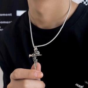 Close-up of retro silver cross pendant with intricate rose detailing on a black t-shirt