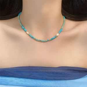 Detail view of turquoise and freshwater pearl necklace worn by a model in soft lighting