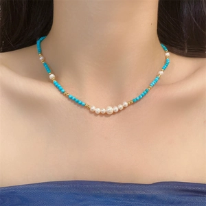Detail of turquoise beads and freshwater pearls necklace on female neck with blue fabric