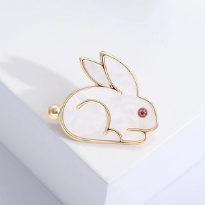 Macro view of cute gold rabbit brooch featuring white shell inlay and pink crystal eye