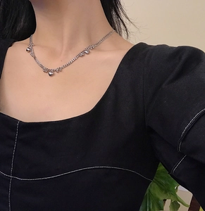 Detail of silver heart charm necklace on model neck highlighting sleek metal link design
