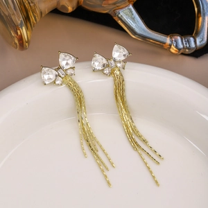 Detailed close-up of gold tassel earrings with crystal bow on a white ceramic plate