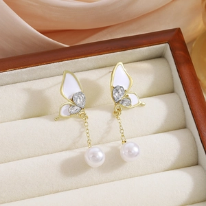Macro view of butterfly earrings with white enamel wings and hanging pearls