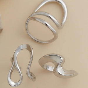 Detailed view of three minimalist silver irregular molten lava design rings on beige background