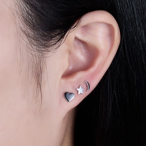 Detail view of silver heart, star, and crescent moon stud earrings worn on ear
