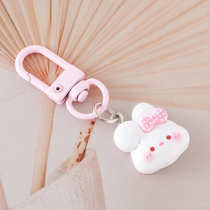 Dettaglio portachiavi a forma di coniglio bianco con fiocco rosa su sfondo beige chiaro