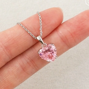 Macro shot of pink heart-shaped crystal necklace held between fingers for scale