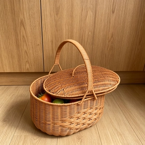 Close-up of a woven picnic basket with dual lid and round handle holding fresh fruit