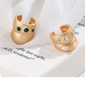 Detailed shot of matte gold ear cuffs with green gems and pearls on white fabric background
