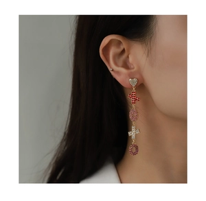 Close-up of dangling heart and cross earrings with colorful rhinestones on model