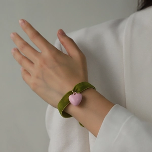Grünes Samt-Armband mit rosa Herz-Anhänger am Handgelenk für einen trendigen Look