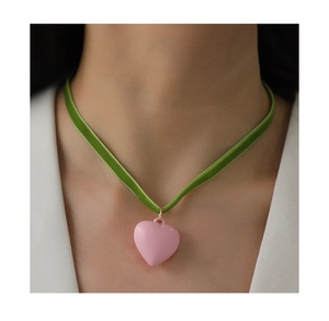 Dettaglio del choker in velluto verde con ciondolo a cuore rosa opaco e anello d'oro