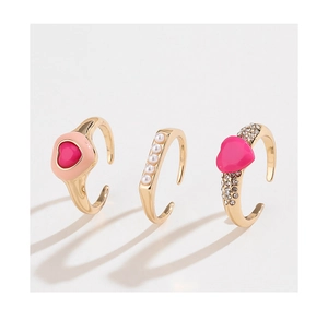 Detail of three-piece gold ring set featuring pink hearts and white pearls on white background