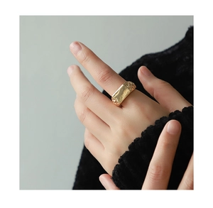 Detail of wide gold ring with rectangular hammered texture and woven cutout patterns