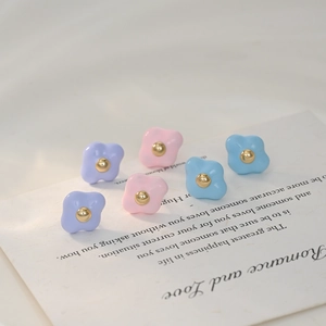 Macro detail of sweet macaron flower earrings with gold bead center on paper background