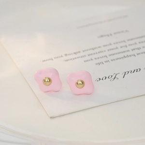 Close-up of pink enamel floral stud earrings with a golden center bead on card