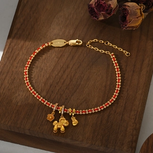 Detail of red woven bracelet with gold pig, flower and money bag charms on wood