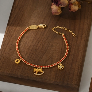 Macro detail of red woven bracelet with gold rocking horse charm and coin pendants